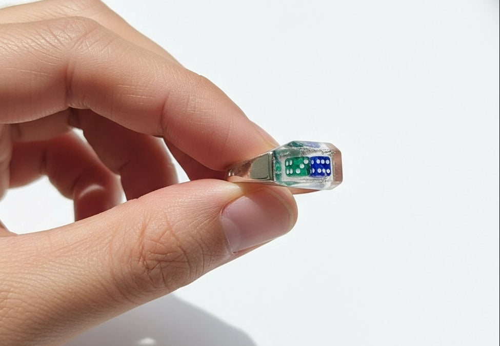 Hand holding a clear resin ring with 2 die embedded